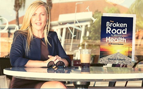 Sharon sitting at table posing with her book The Broken Road to Mental Health
